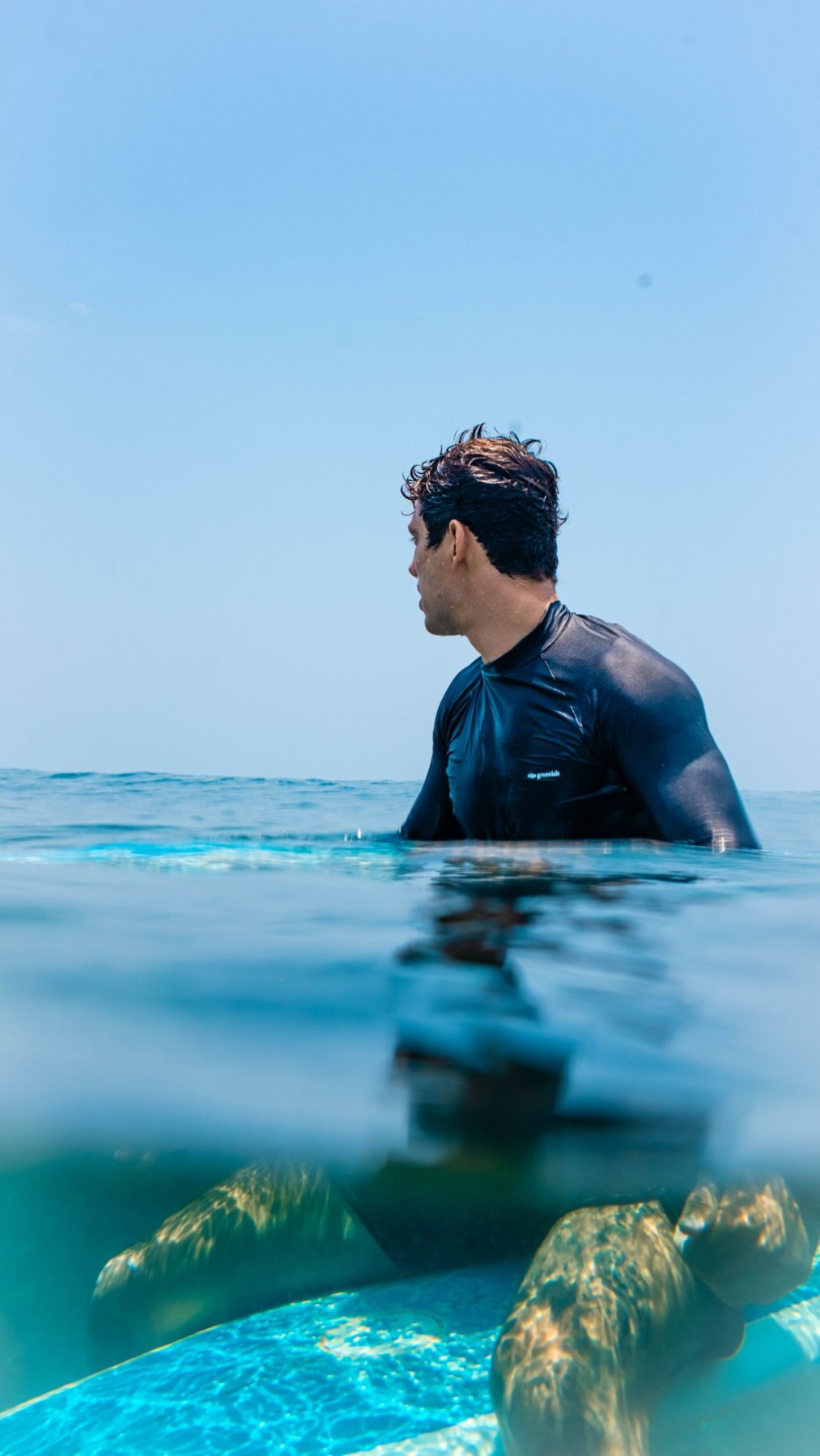 A surfer looking out to sea, half in half out of the water